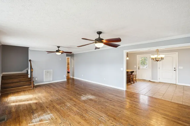 an empty room with wooden floor chandelier fan and windows