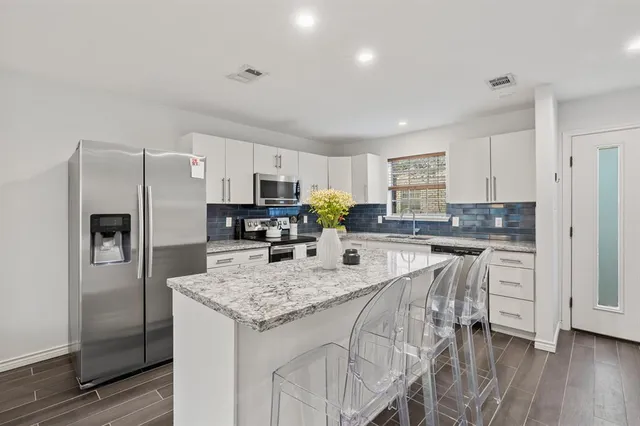 a kitchen with granite countertop stainless steel appliances a refrigerator a stove top oven and sink