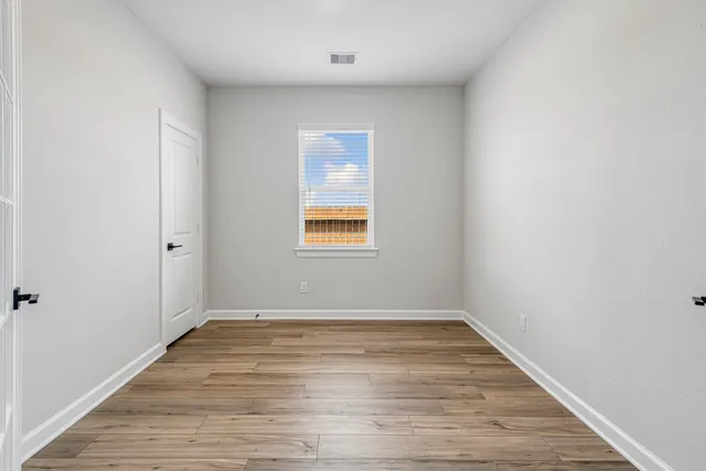 a view of an empty room with wooden floor and a window