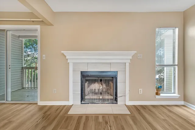 a view of an empty room with wooden floor fireplace and a window