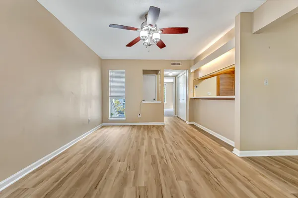 an empty room with wooden floor chandelier fan and windows