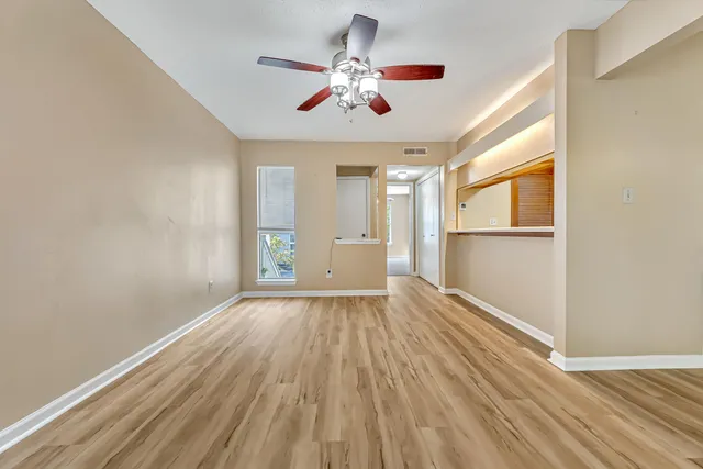 an empty room with wooden floor chandelier fan and windows