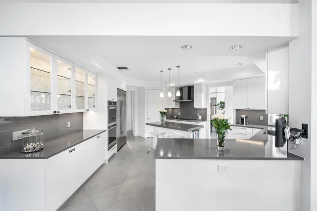 a large white kitchen with stainless steel appliances granite countertop a lot of cabinets a sink and a counter top space