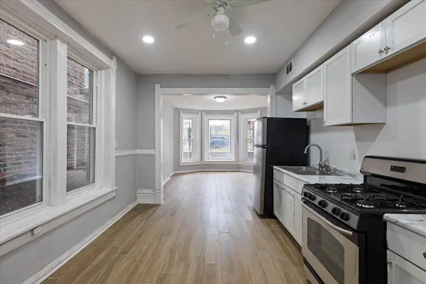 a kitchen with stainless steel appliances granite countertop a stove top oven a sink dishwasher a refrigerator and white cabinets with wooden floor