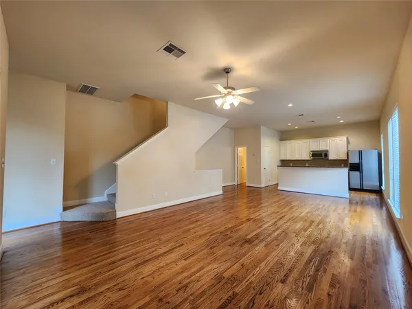 a view of an empty room and kitchen with wooden floor