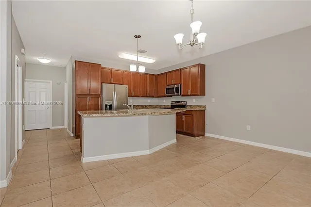 a kitchen with kitchen island granite countertop stainless steel appliances cabinets a sink and a chandelier