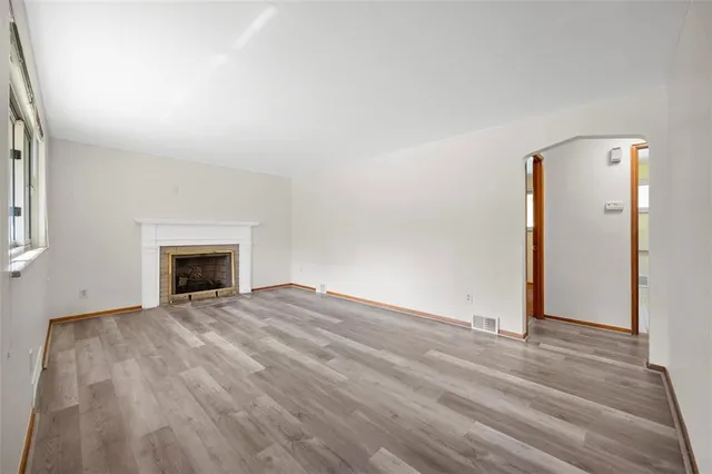 an empty room with wooden floor fireplace and hallway