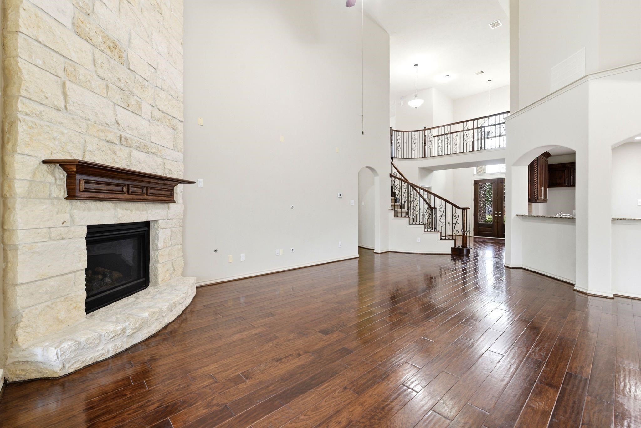 19903 Senterra Lakes Boulevard Spring, TX 77379 - Photo 8 of 50 Spacious living area with rich hardwood floors, a striking stone fireplace, and elegant wrought iron staircase, offering an inviting atmosphere.