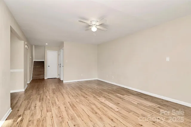 a view of an empty room with wooden floor and a ceiling fan