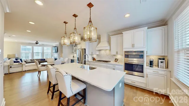 a kitchen with stainless steel appliances kitchen island granite countertop a stove a sink a oven a dining table and chairs with wooden floor