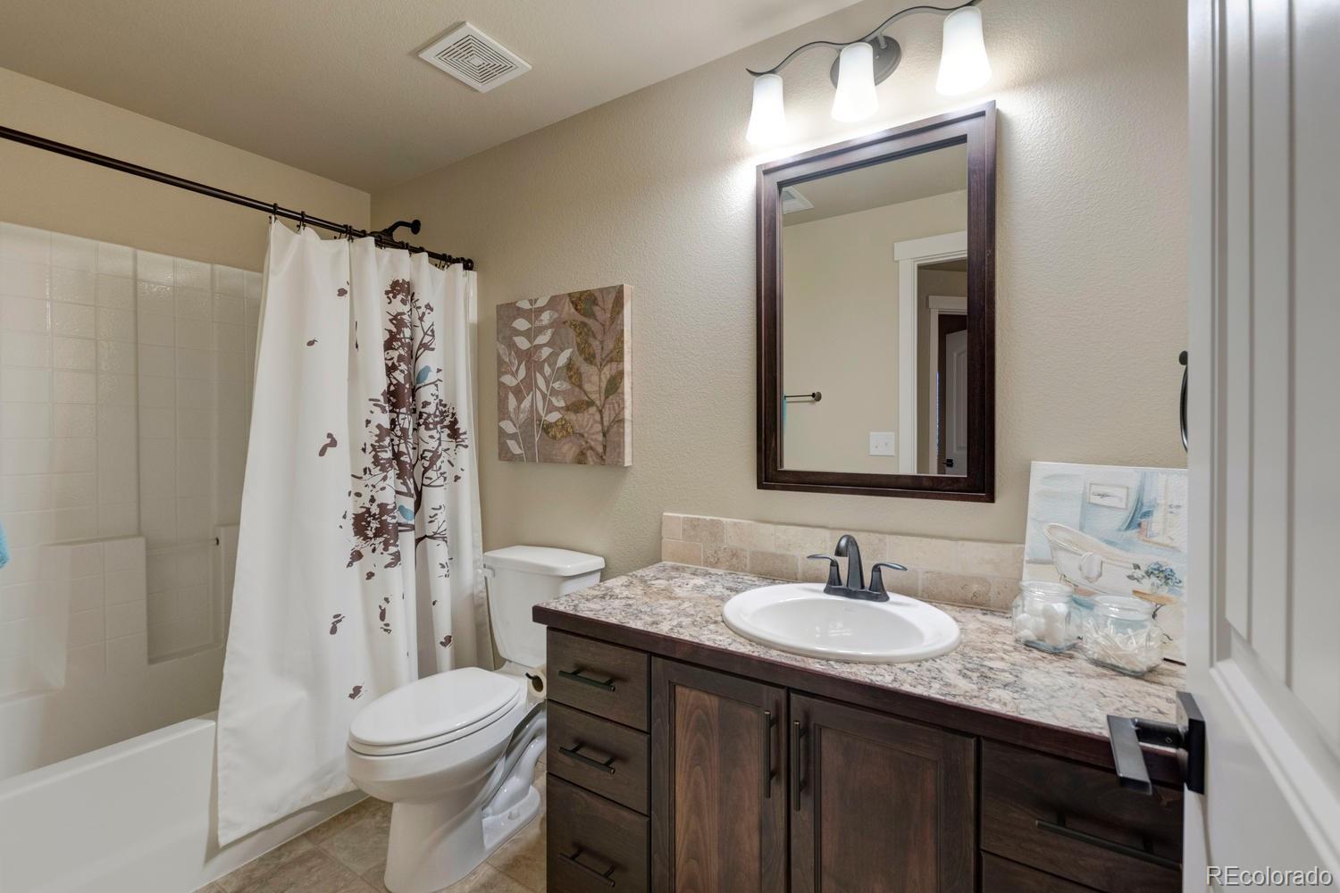 4188 Meadowlark Road Fort Lupton, CO 80621 - Photo 28 of 36 a bathroom with a granite countertop sink toilet a mirror a vanity and shower