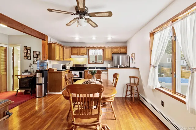 a dining room with stainless steel appliances a dining table wooden floor and a large window