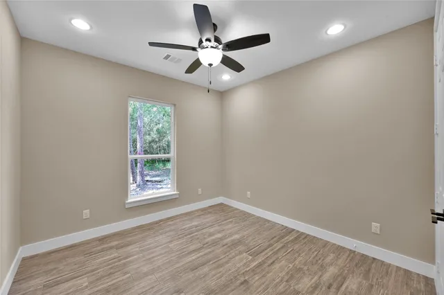 an empty room with wooden floor fan and windows