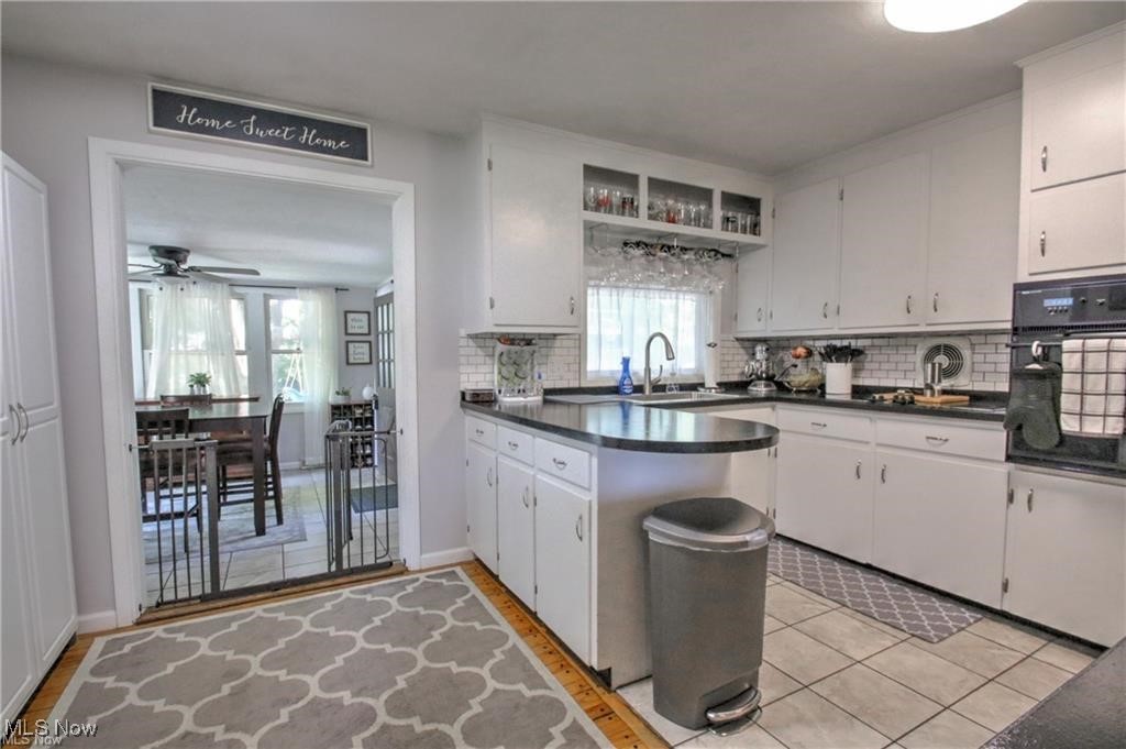 Kitchen featuring a sink, decorative backsplash, oven, a ceiling fan, and dark countertops