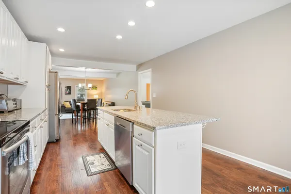 a kitchen with granite countertop a stove top oven a sink dishwasher and a refrigerator with wooden floor