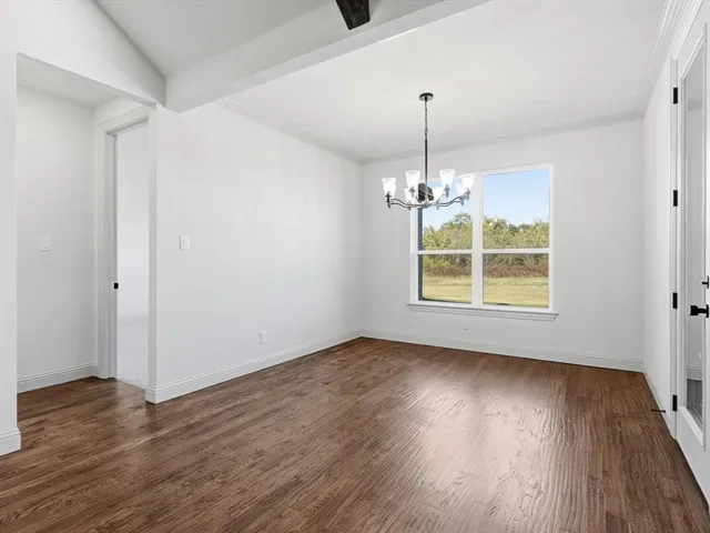 an empty room with wooden floor chandelier and windows