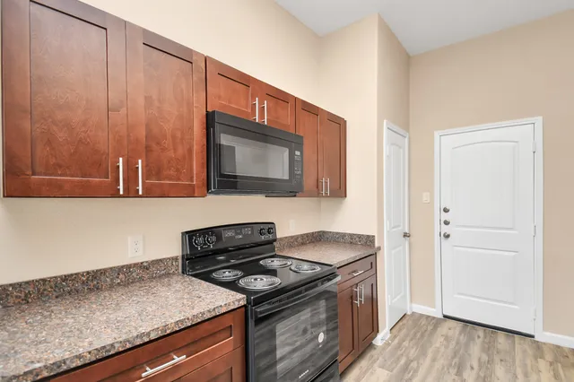 a kitchen with granite countertop a stove top oven microwave and cabinets with wooden floor