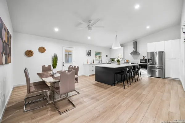 a dining hall with stainless steel appliances kitchen island granite countertop a dining table chairs and a refrigerator
