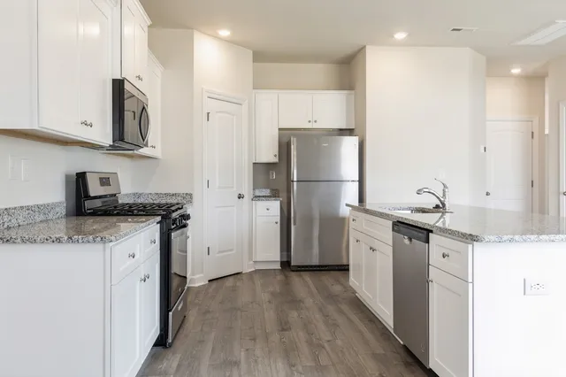 a kitchen with stainless steel appliances granite countertop a refrigerator a stove a sink and white cabinets with wooden floor