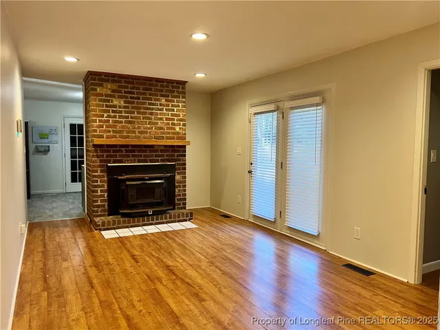 a view of an empty room with wooden floor a fireplace and a window
