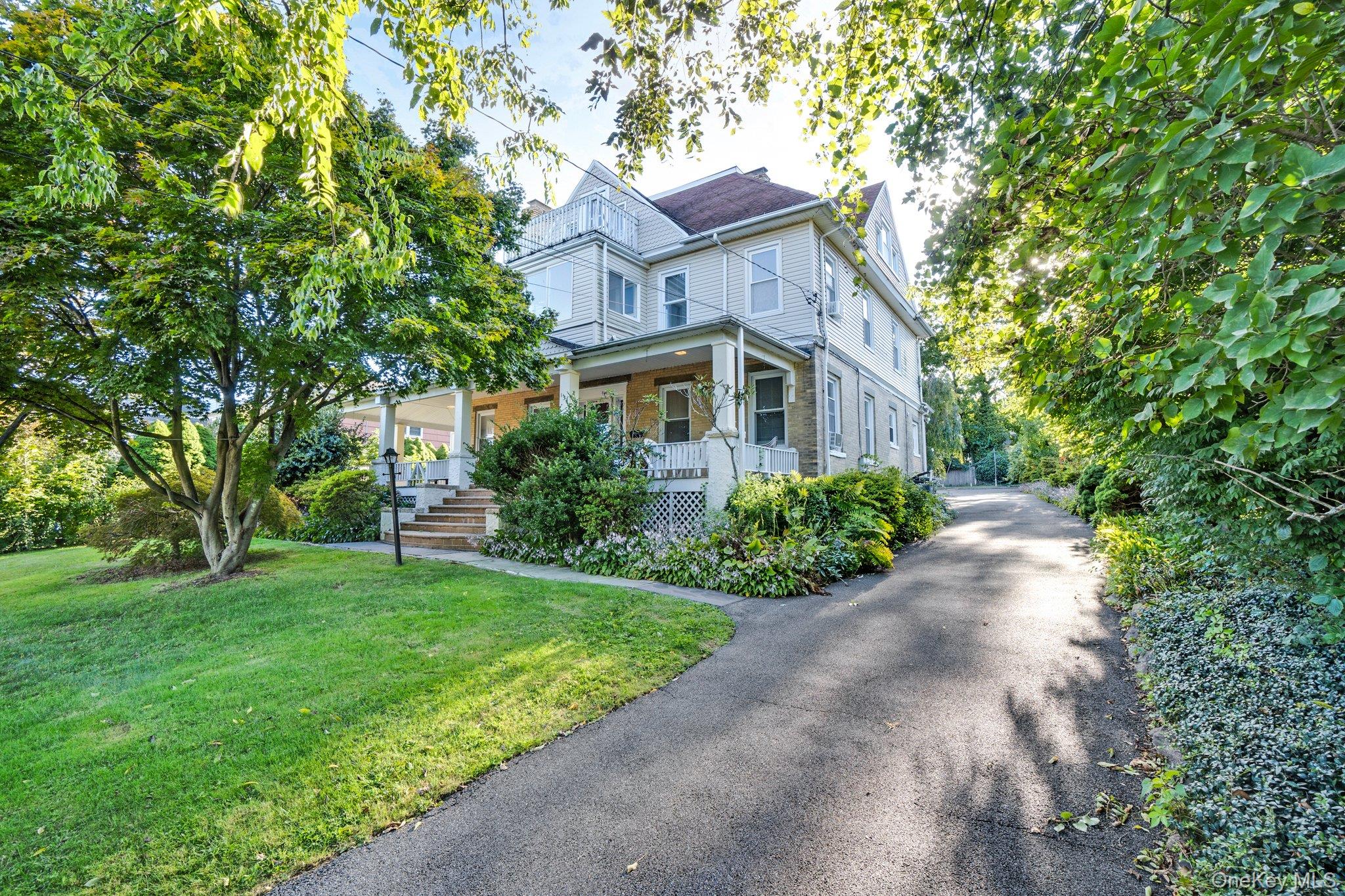 a view of a brick house with a big yard plants and large trees