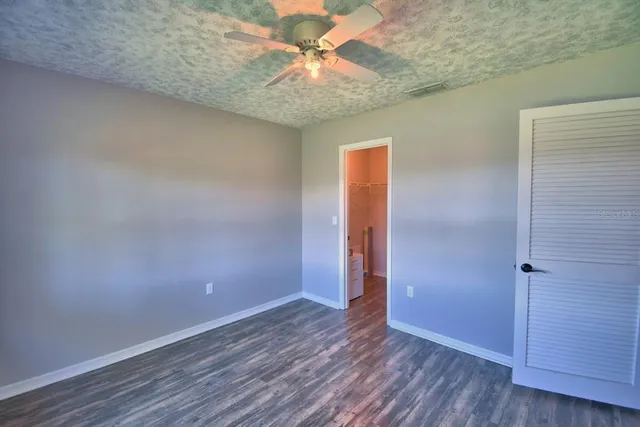 an empty room with a chandelier fan and wooden floor