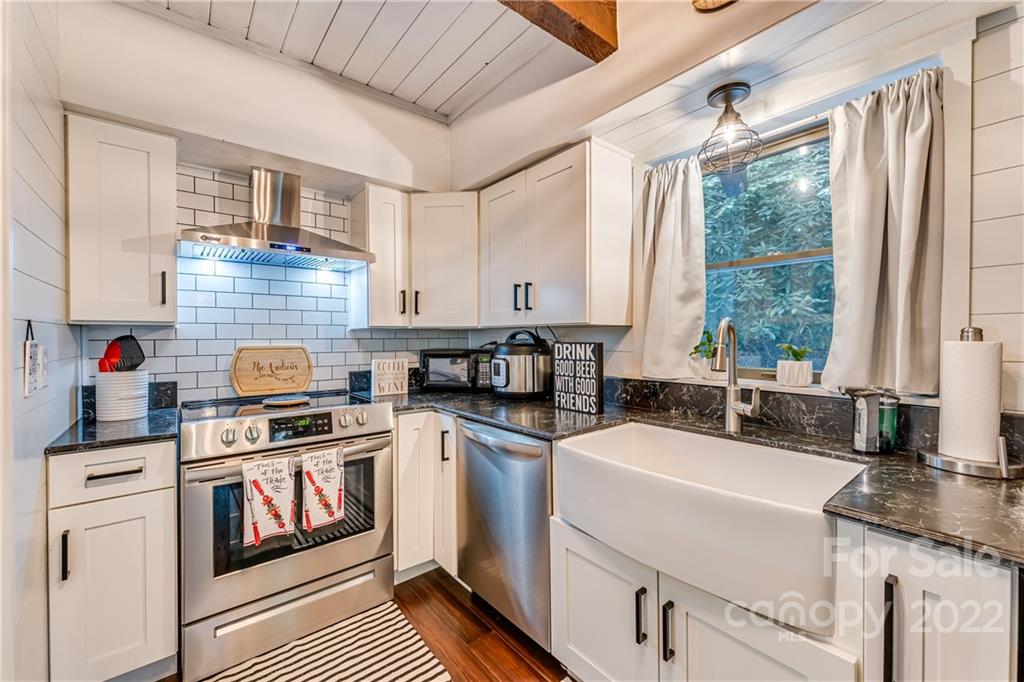 1305 Old Balsam Road Waynesville, NC 28786 - Photo 17 of 42 a kitchen with stainless steel appliances granite countertop a stove a sink dishwasher and white cabinets with wooden floor