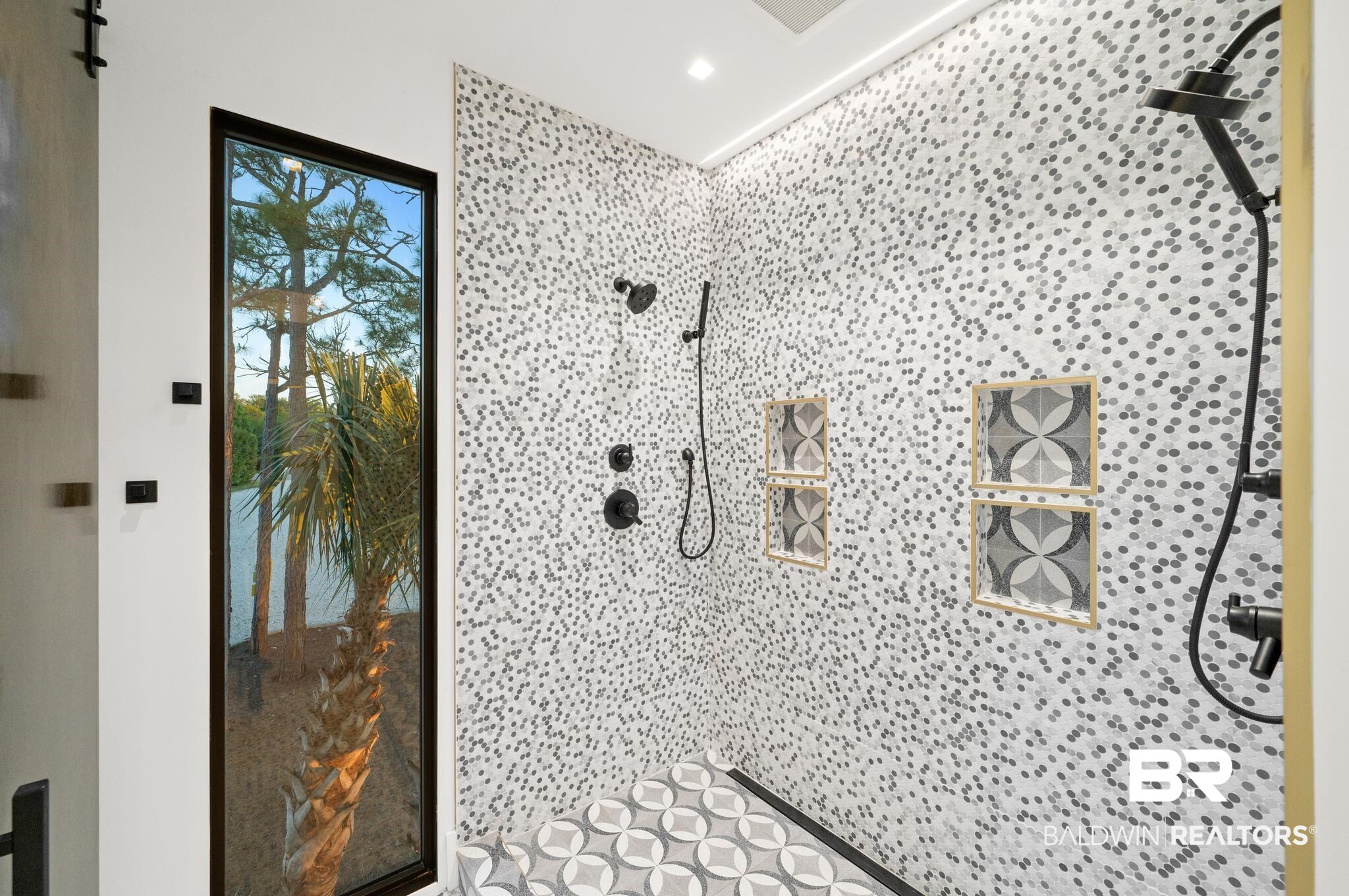 33349 River Road Orange Beach, AL 36561 - Photo 26 of 61 Tiled shower enclosure featuring dual matte black shower heads, integrated niches with patterned tile accents, and a full-height window