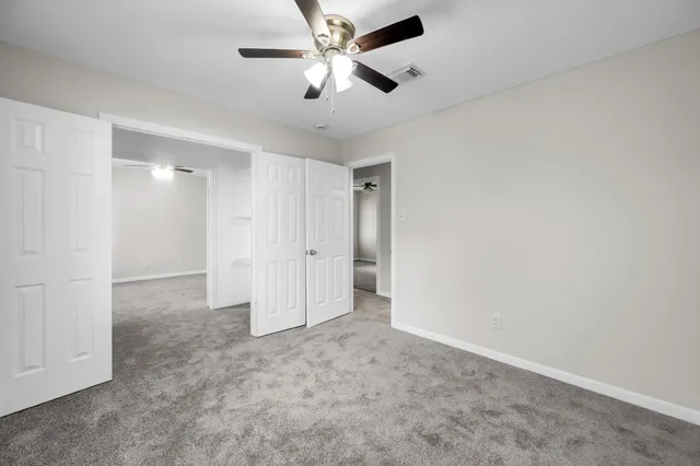 an empty room with chandelier fan and closet area