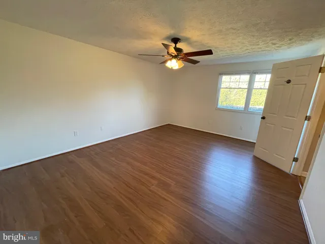 an empty room with wooden floor fan and windows