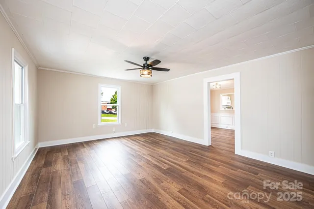 an empty room with wooden floor chandelier fan and windows