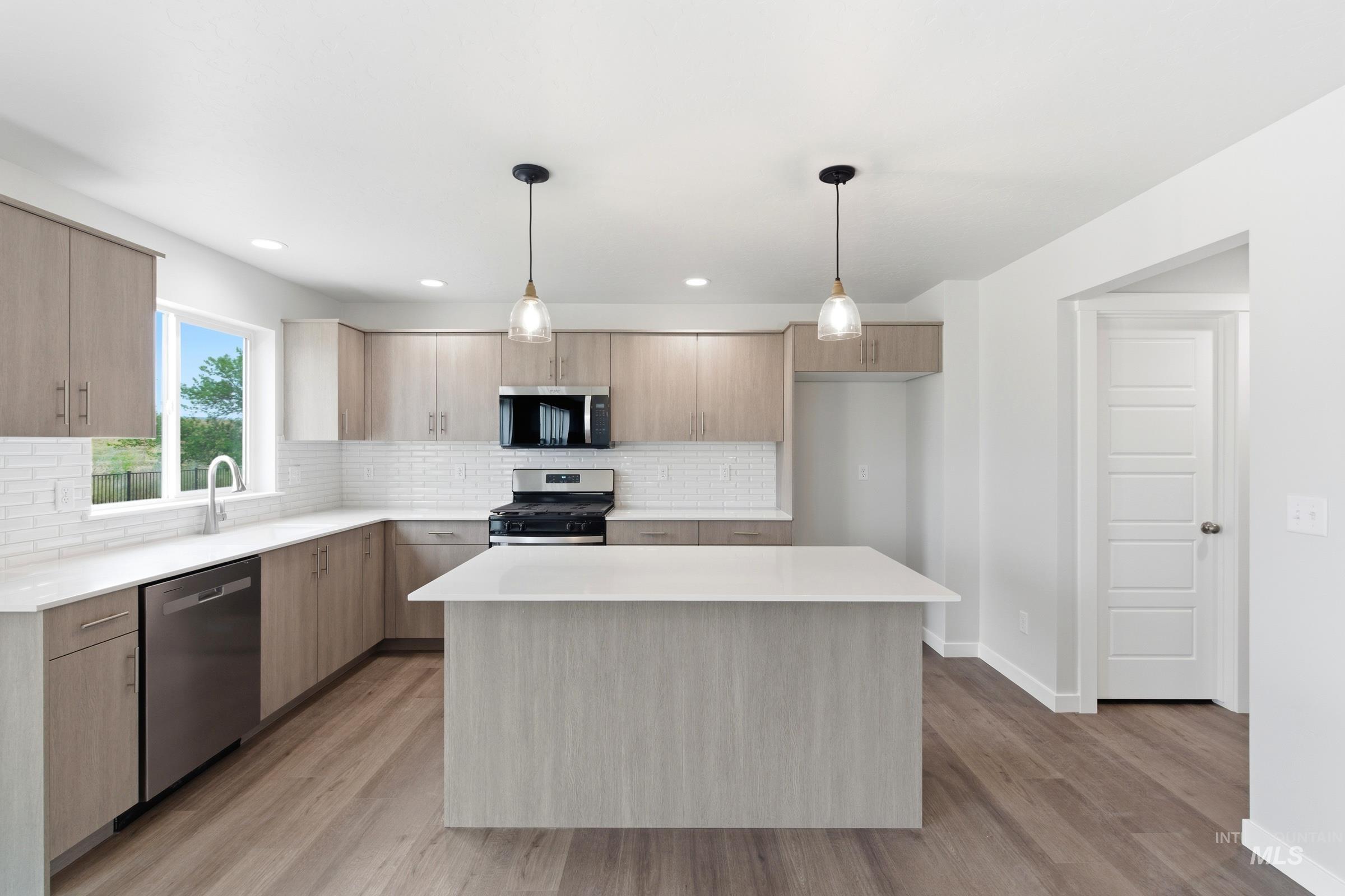 12829 Decatur Street Nampa, ID 83651 - Photo 3 of 33 Modern kitchen featuring wood-finish cabinetry, white countertops, a subway tile backsplash, and stainless steel appliances including a gas range and dishwasher