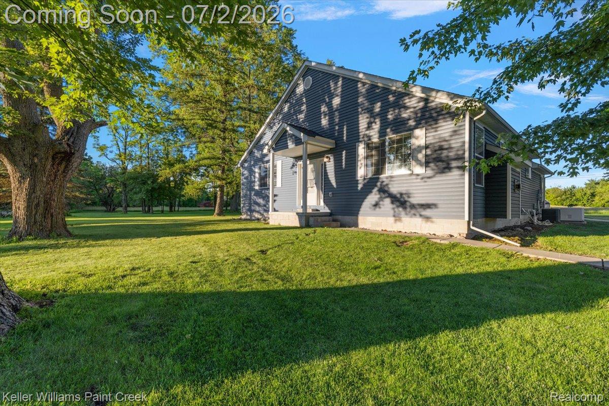 54230 Card Road Macomb, MI 48042 - Photo 3 of 73 Exterior siding in a gray finish, mature trees, manicured lawn, white window frames, and a concrete foundation