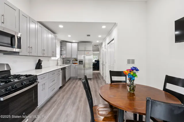 a white kitchen with stainless steel appliances granite countertop a stove a refrigerator a kitchen island a table and chairs