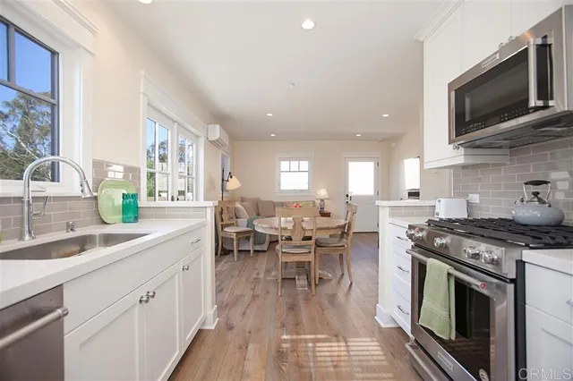 a open kitchen with stainless steel appliances granite countertop a stove top oven a sink dishwasher a dining table and chairs with wooden floor