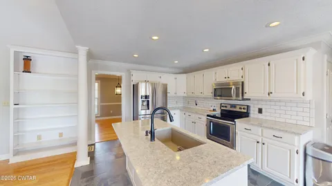 a kitchen with stainless steel appliances granite countertop a stove top oven a sink a refrigerator and white cabinets with wooden floor