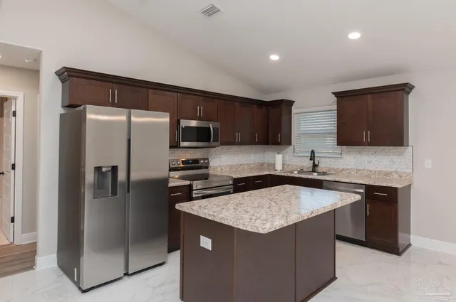 a kitchen with stainless steel appliances granite countertop a refrigerator a sink a stove a microwave and a refrigerator