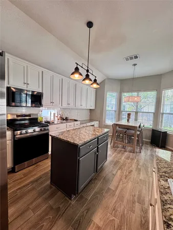 a kitchen with kitchen island granite countertop a stove top oven a sink dishwasher a dining table and chairs with wooden floor