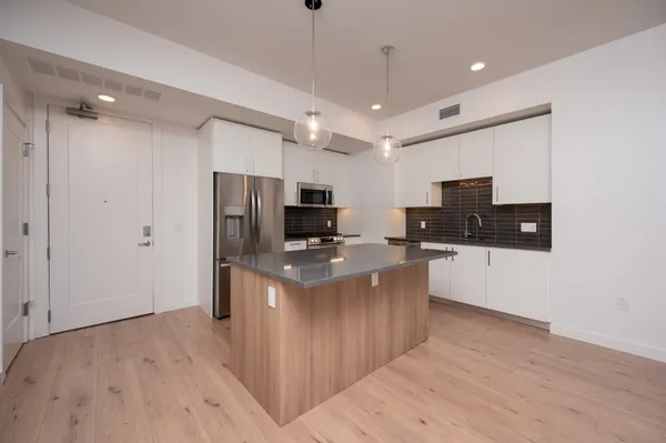 a kitchen with stainless steel appliances a stove top oven a sink a refrigerator a center island and wooden floor