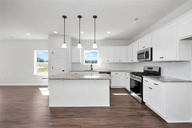 a large kitchen with stainless steel appliances kitchen island granite countertop a sink a stove a refrigerator and white cabinets