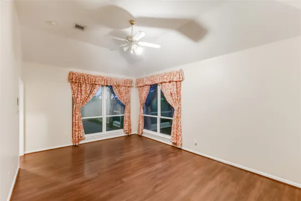 an empty room with wooden floor fan and windows