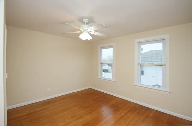an empty room with wooden floor fan and windows