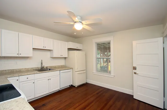 a kitchen with a sink dishwasher and white cabinets with wooden floor