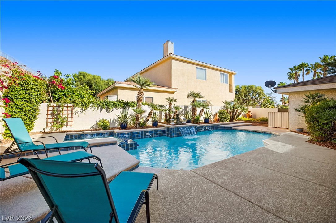 1135 Calico Ridge Drive Henderson, NV 89011 - Photo 48 of 86 A tranquil backyard oasis featuring a sparkling pool with water features, surrounded by mature landscaping and a private stucco wall.