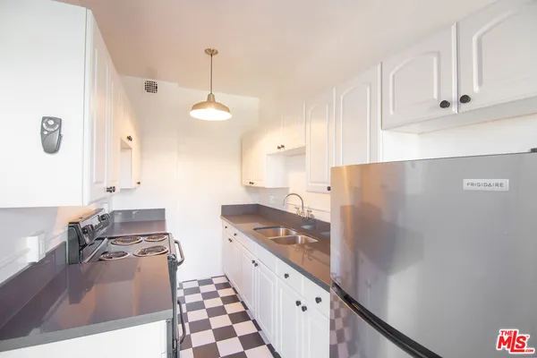 a kitchen with granite countertop a refrigerator a stove and white cabinets