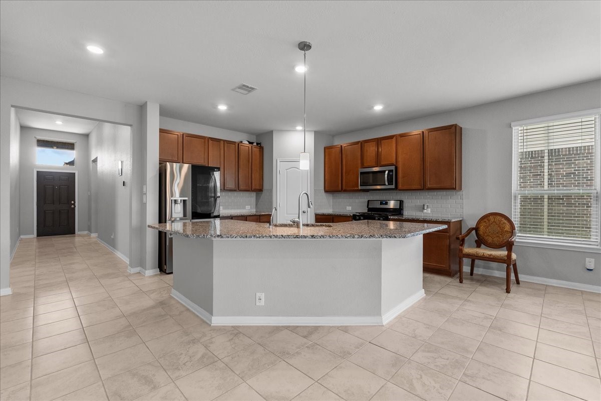 2320 Rosemary Street Rosenberg, TX 77469 - Photo 14 of 40 This photo showcases a modern kitchen with an open layout, featuring a large island with granite countertops, stainless steel appliances, and ample cabinet space. The space is bright with recessed lighting and a large window, complemented by neutral tile flooring.