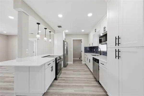 a large kitchen with stainless steel appliances kitchen island a large counter top a stove a chimney a sink and a refrigerator