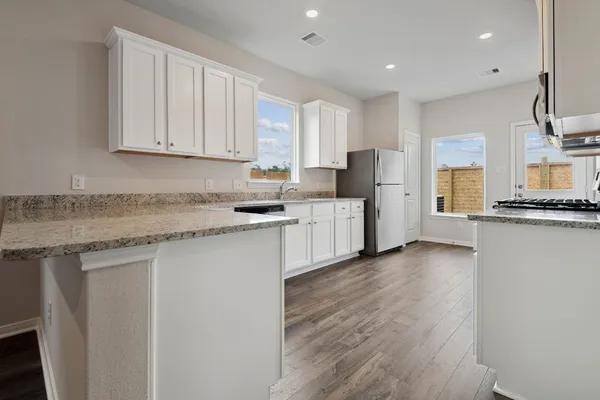 a kitchen with stainless steel appliances granite countertop a stove a refrigerator a sink and white cabinets with wooden floor