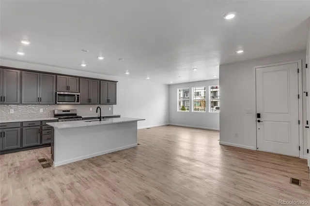 a kitchen with stainless steel appliances granite countertop a stove top oven a sink dishwasher and a refrigerator with wooden floor