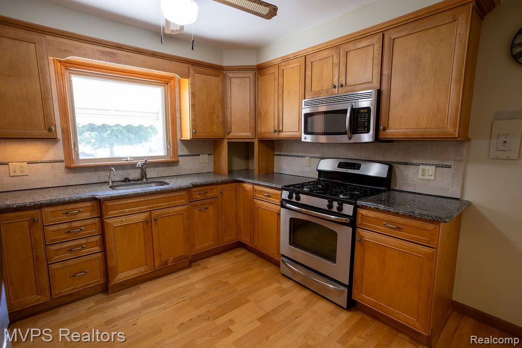 33033 Edgegrove Road Fraser, MI 48026 - Photo 9 of 20 Full kitchen featuring wood cabinetry, dark speckled countertops, stainless steel appliances, tile backsplash, and wood-finish flooring
